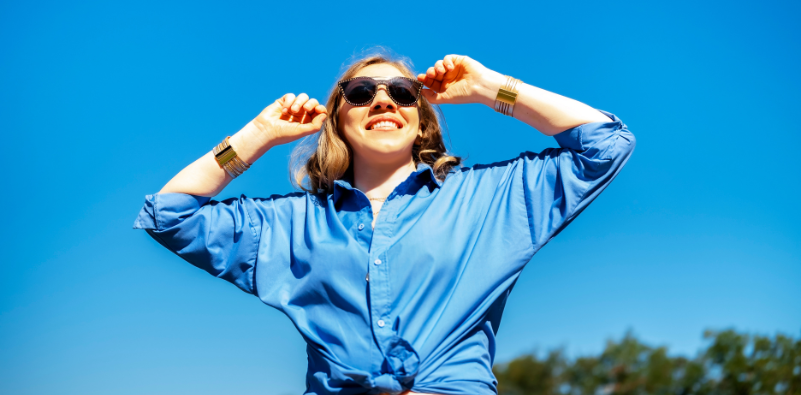 Woman smiling wearing sunglasses beneath a bright blue summer sky