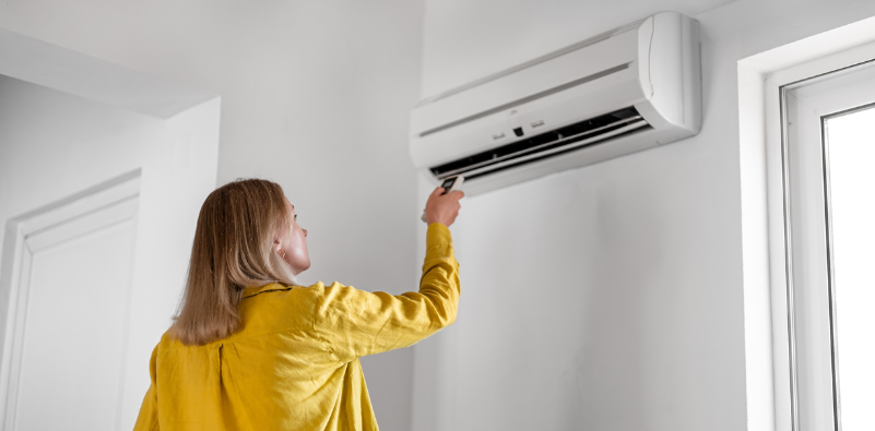 Woman adjusting a wall-mounted air conditioner at home.