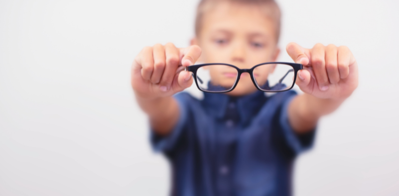 A young boy holding a pair of black glasses towards the camera