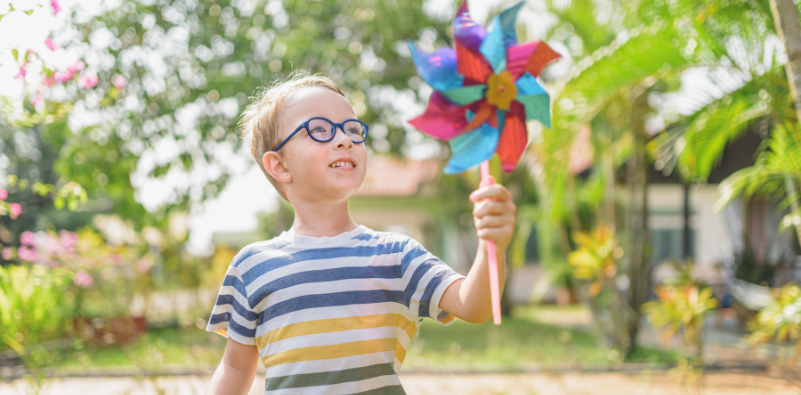Young boy wearing glasses and holding a colourful pinwheel outdoors