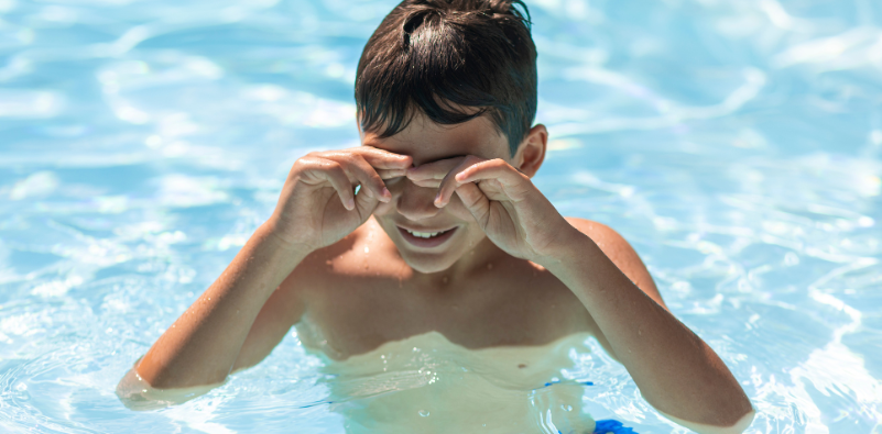 Boy rubbing his eyes while swimming in a pool