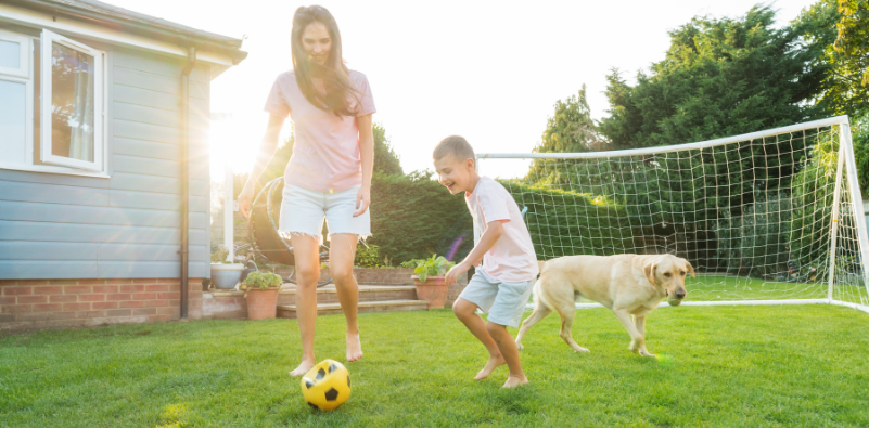 Mother and son playing football with their dog in the garden