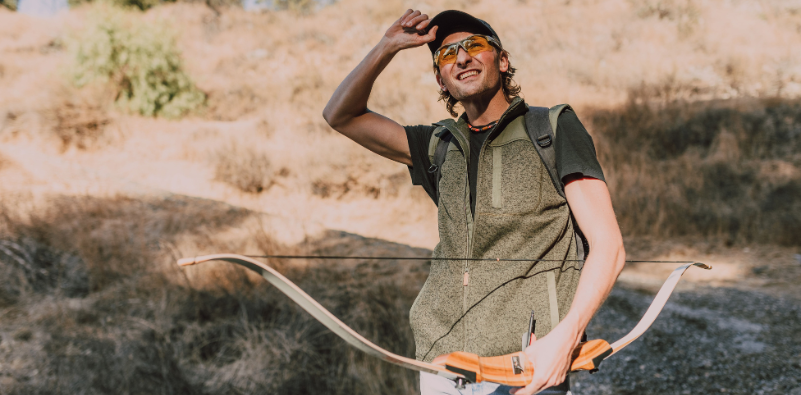 Archer wearing protective sports eyewear and holding a bow outdoors