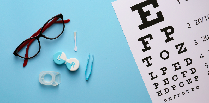 Glasses, contact lenses and accessories arranged beside a Snellen chart on a blue surface.