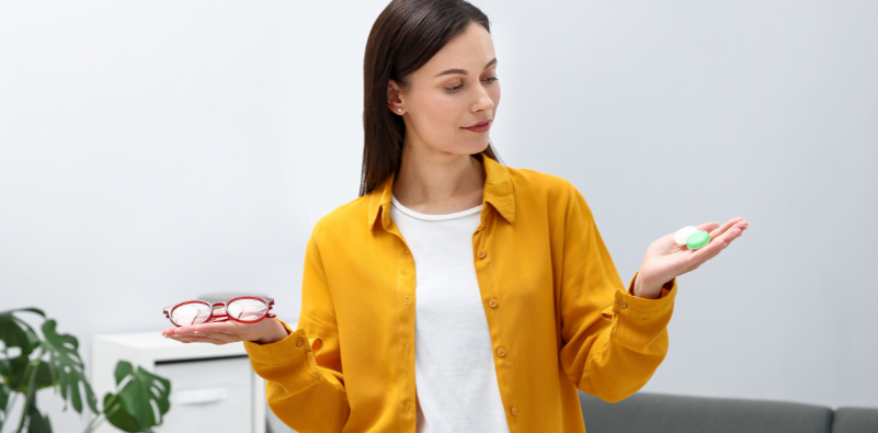 Woman holding a pair of red glasses in one hand and a contact lens case in the other.