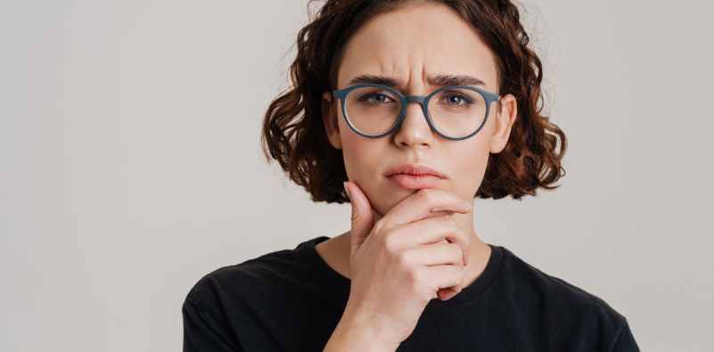 Woman wearing blue glasses with a thoughtful expression and her hand on her chin.