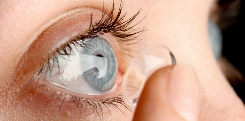 Close-up of a contact lens being placed onto a blue eye.